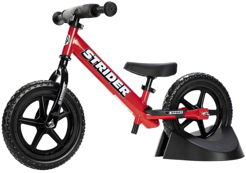 Red Strider balance bike standing upright in a black bike stand