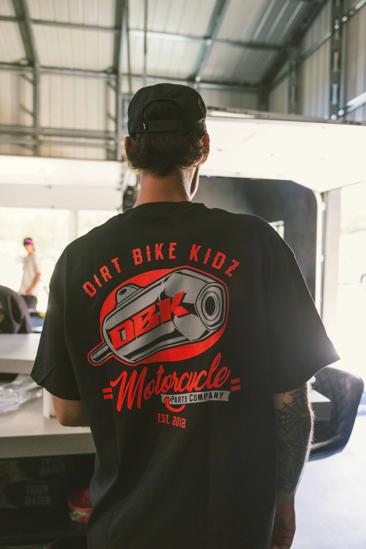 Person in a shop wearing the black DBK Factory tee, back graphic visible