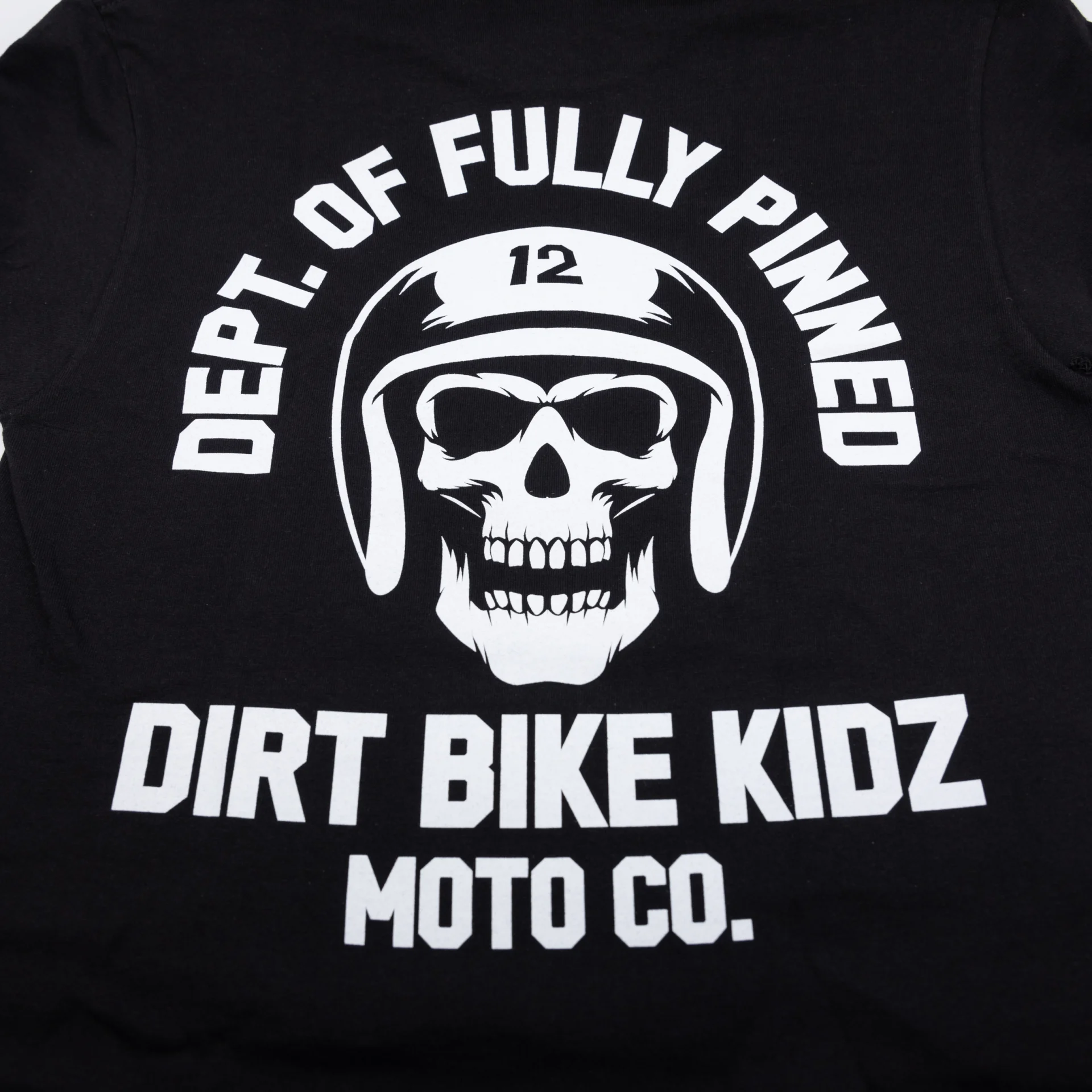 Close-up of the white skull and Dirt Bike Kidz Moto Co. graphic on the black DBK Fully Pinned tee