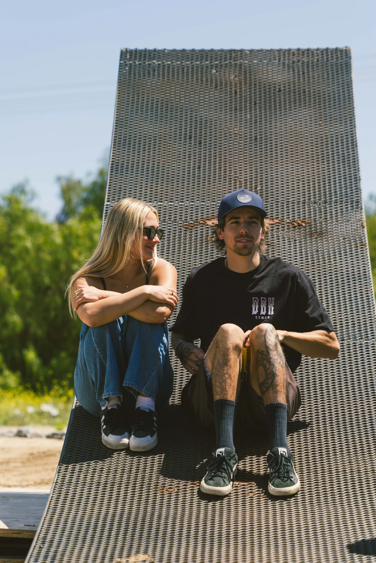 Two people sitting on a wooden ramp, one wearing the DBK Ghost Rider Tee in black