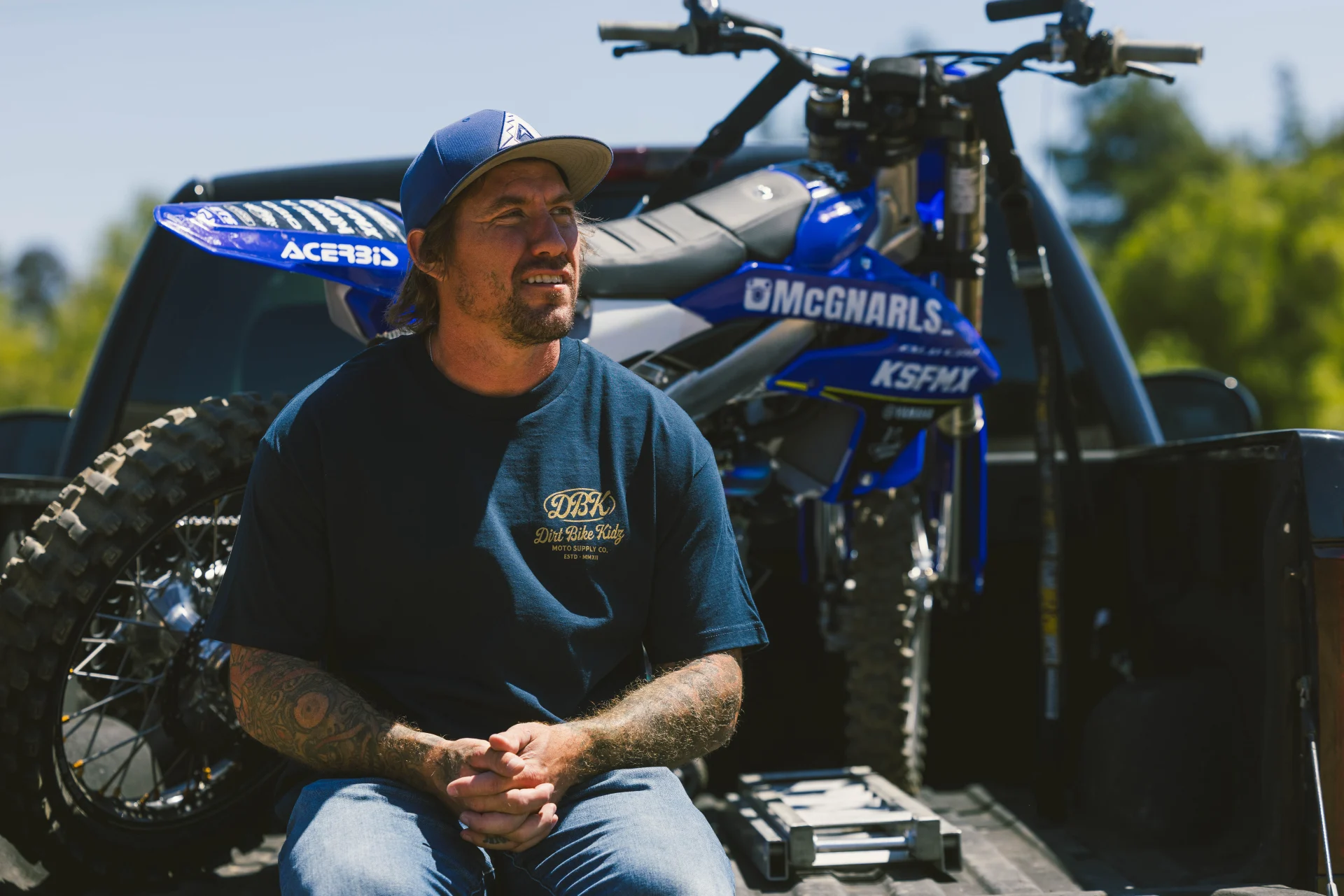 Man in the DBK Gold Nugget Tee in navy, seated in front of a dirt bike