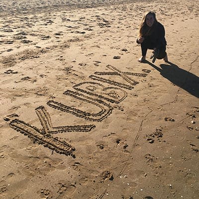 Bethany on a beach with 'KUBIX' scratched into the sand