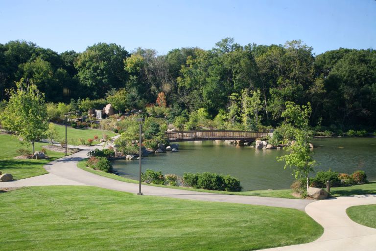 view of path around pond with bridge and trees in background at Rosecrance Griffin Williamson Campus