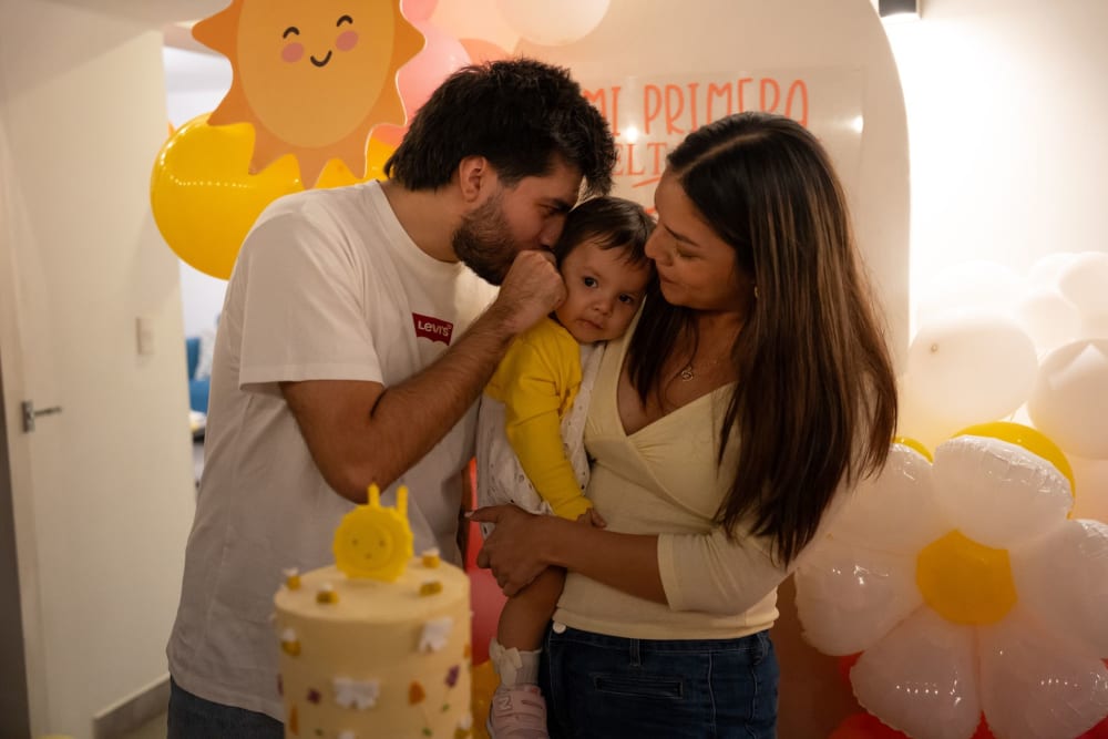 Fotografía de cumpleaños infantil en Lima: papá y mamá besan a Zoe entre globos amarillos