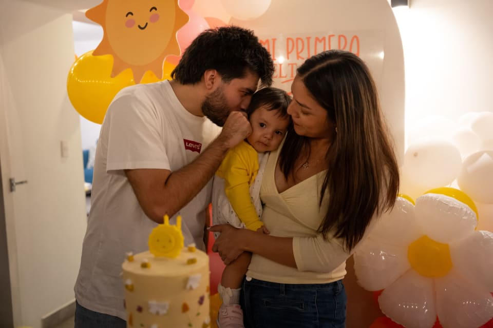 Fotografía de cumpleaños infantil en Lima: papá y mamá besan a Zoe entre globos amarillos
