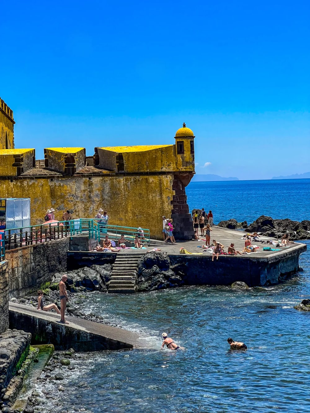 People swimming at Praia de São Tiago beach in the front of the large yellow historic fort