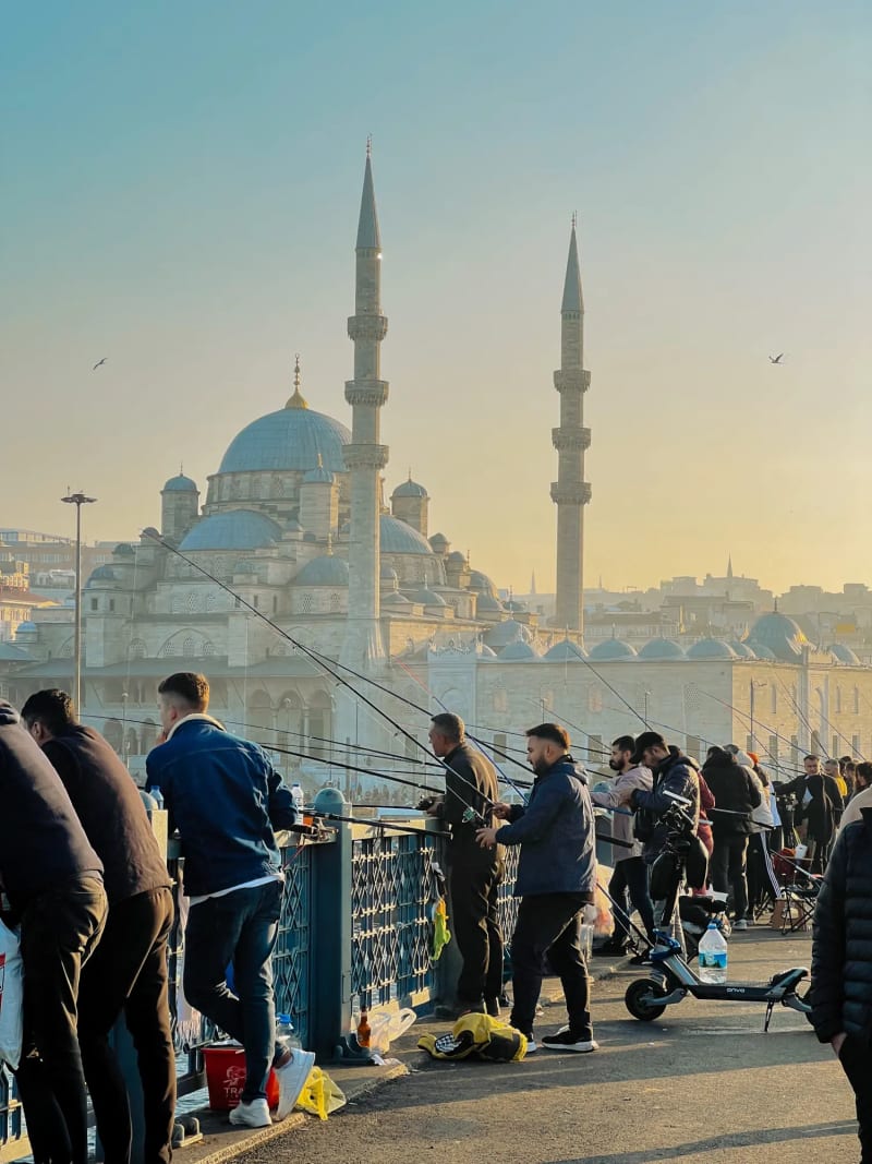 Fisherman on the Galata Bridge with a mosque in the distance in Istanbul Turkey