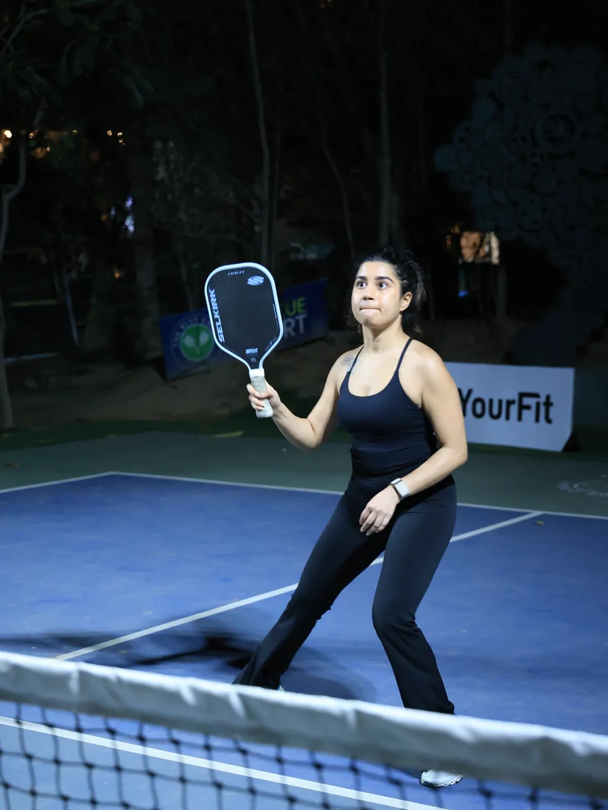 A player strikes a return under lights at a FindYourFit pickleball match