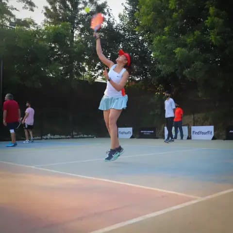 A woman jumping for an overhead smash at a FindYourFit pickleball night