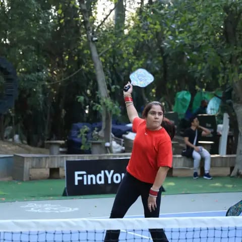 A woman serving overhead at a FindYourFit pickleball night