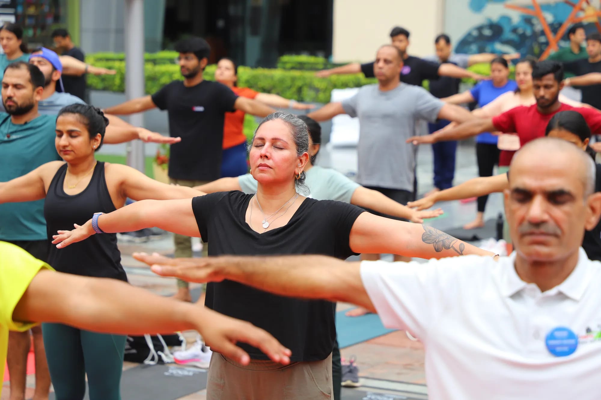 A crowd of participants holding a yoga pose, arms outstretched, eyes closed
