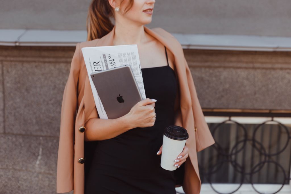 Image of a woman holding a newspaper, a laptop, and a cup of coffee