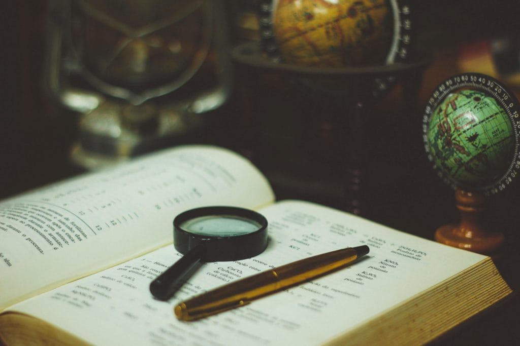 magnifying glass and pen on the top of an open book