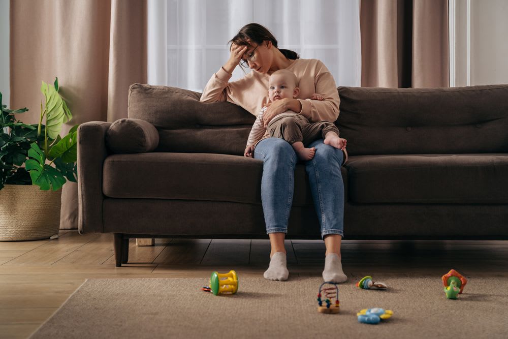 mère épuisée qui porte son bébé dans un salon en désordre