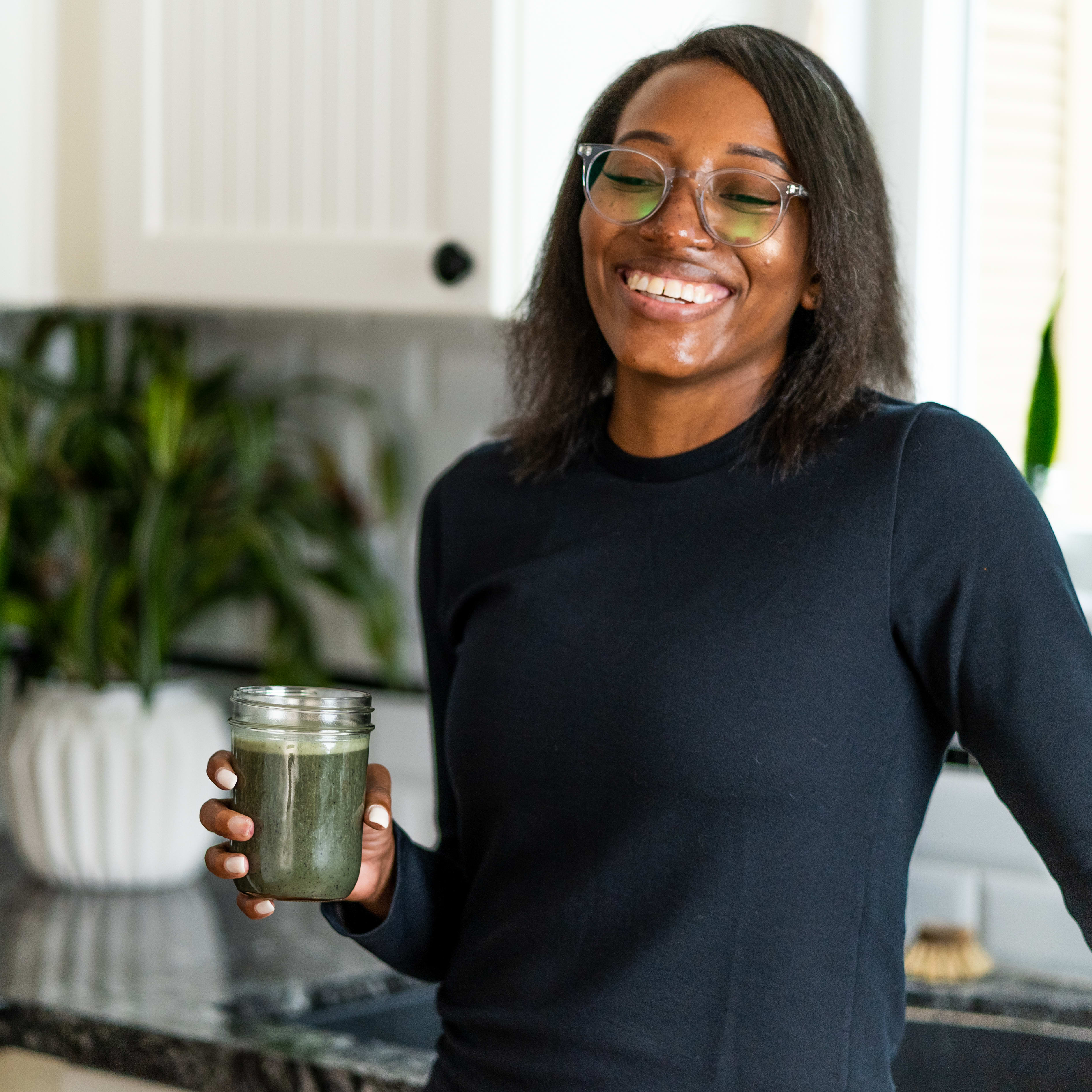 Smiling woman holding a glass with a green smoothy inside.
