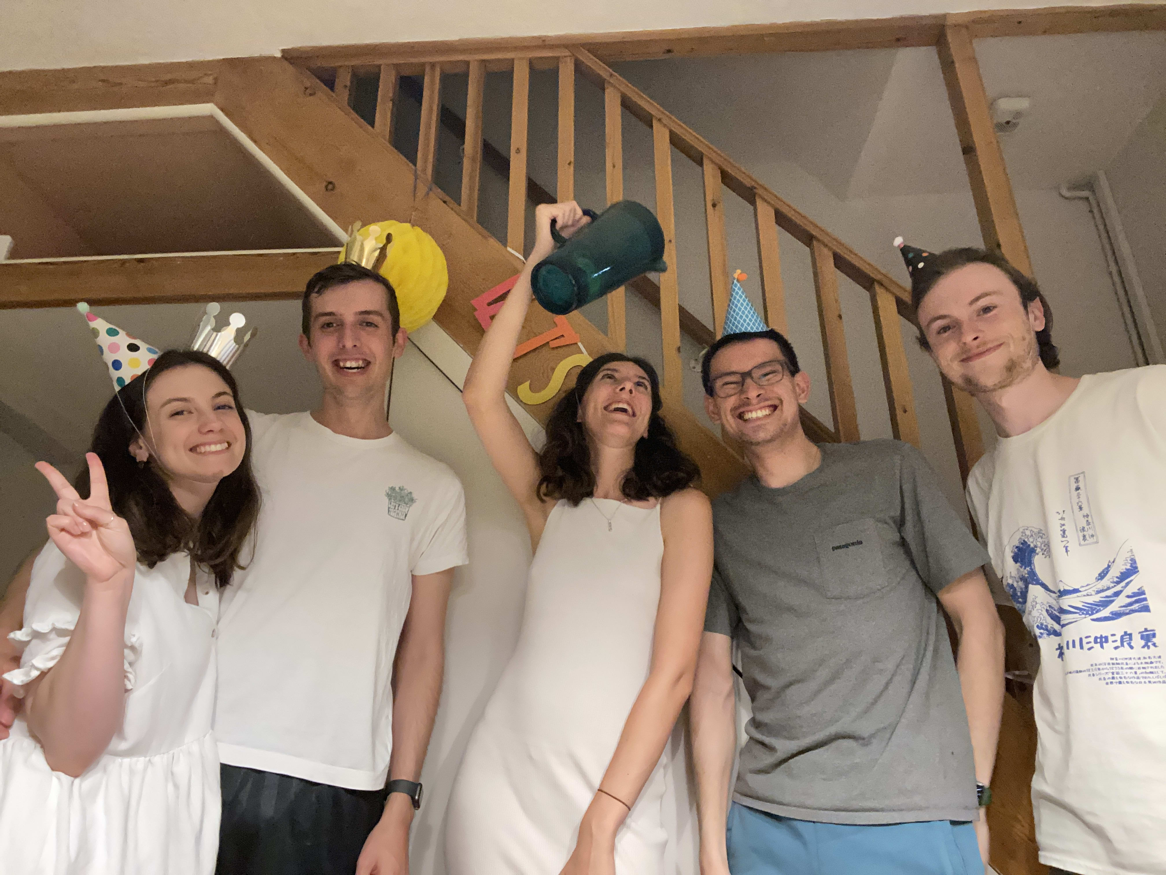 Naomi, Joe, Siobhan, James and Jake all stood in front of the stairs. Naomi, Joe, James and Jake are all smiling and looking at the camera, while Siobhan holds a blue jug of cocktails above James' head as if she's about to pour it, while laughing.