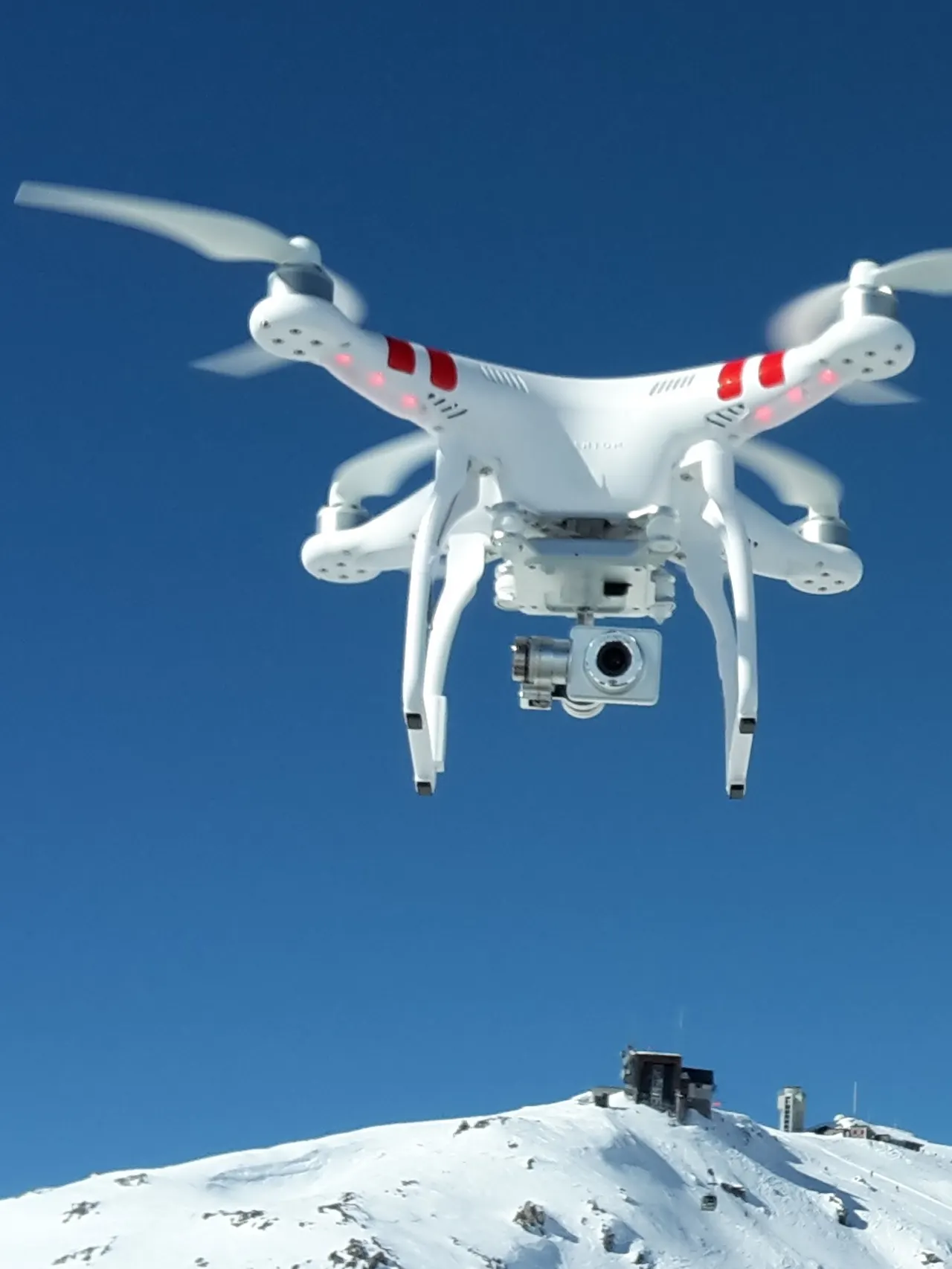 A white drone hovers over a snow covered mountain landscape