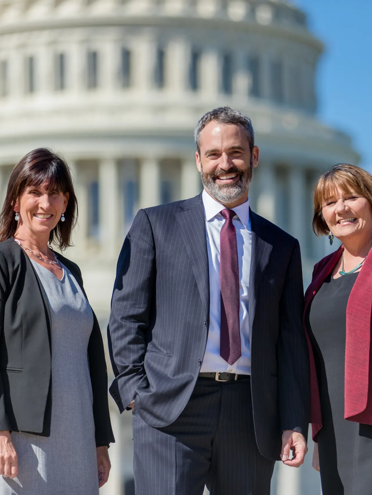 Three people standing in front of the U.S. Capitol smiling.