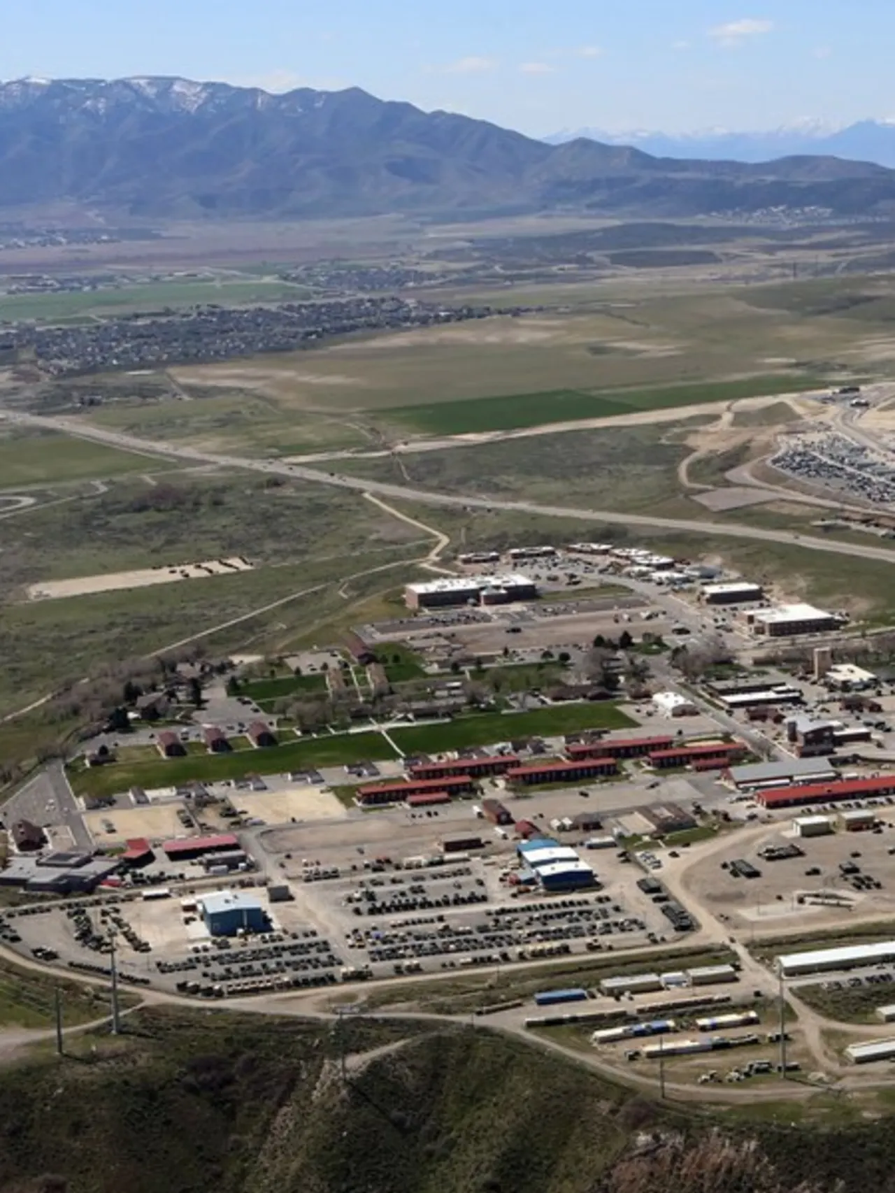 Photo taken from above of a military complex with many buildings and cars, surrounded by forest and mountains.