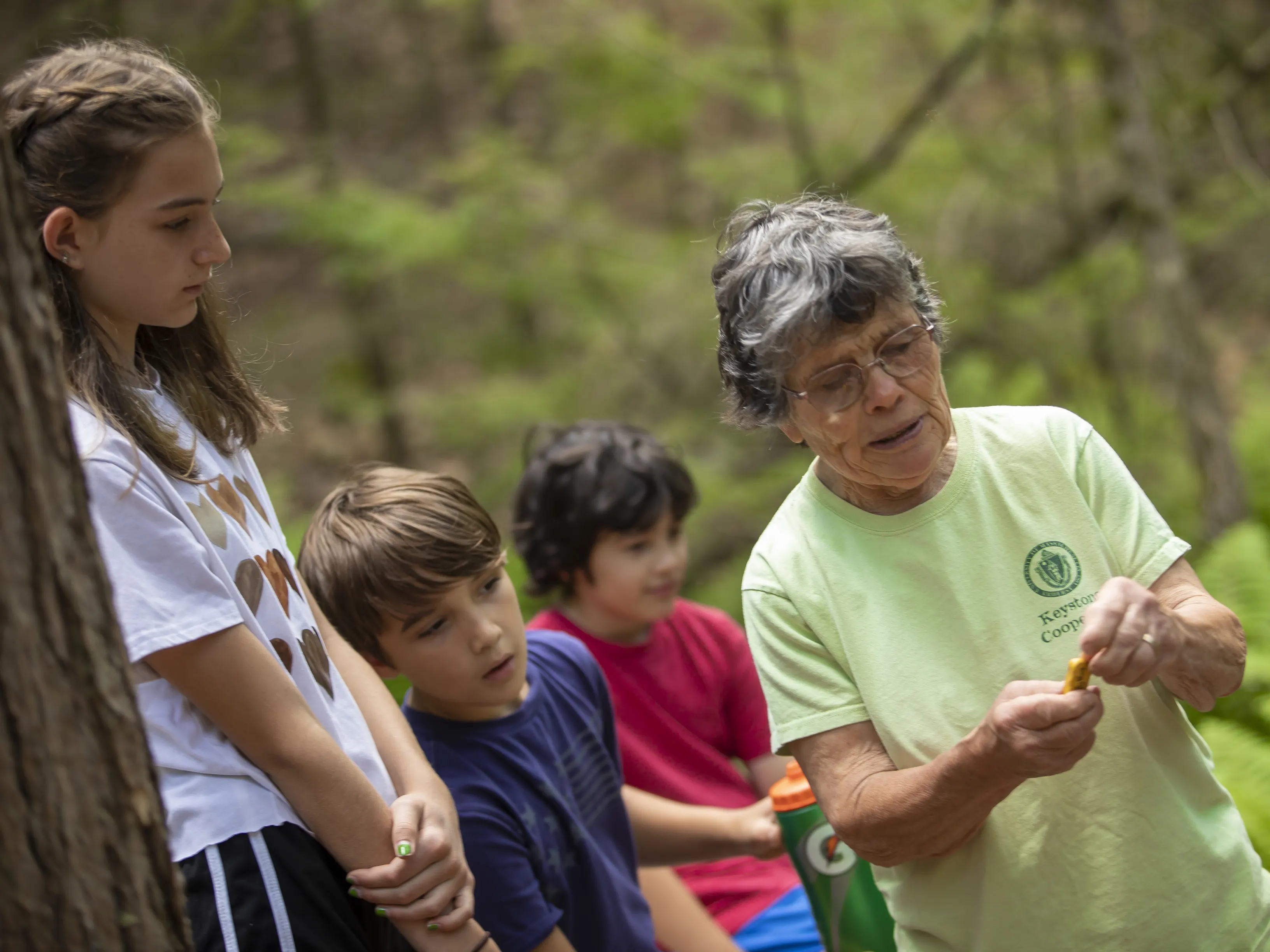 A woman is holding something that she's showing to three children looking over her shoulder