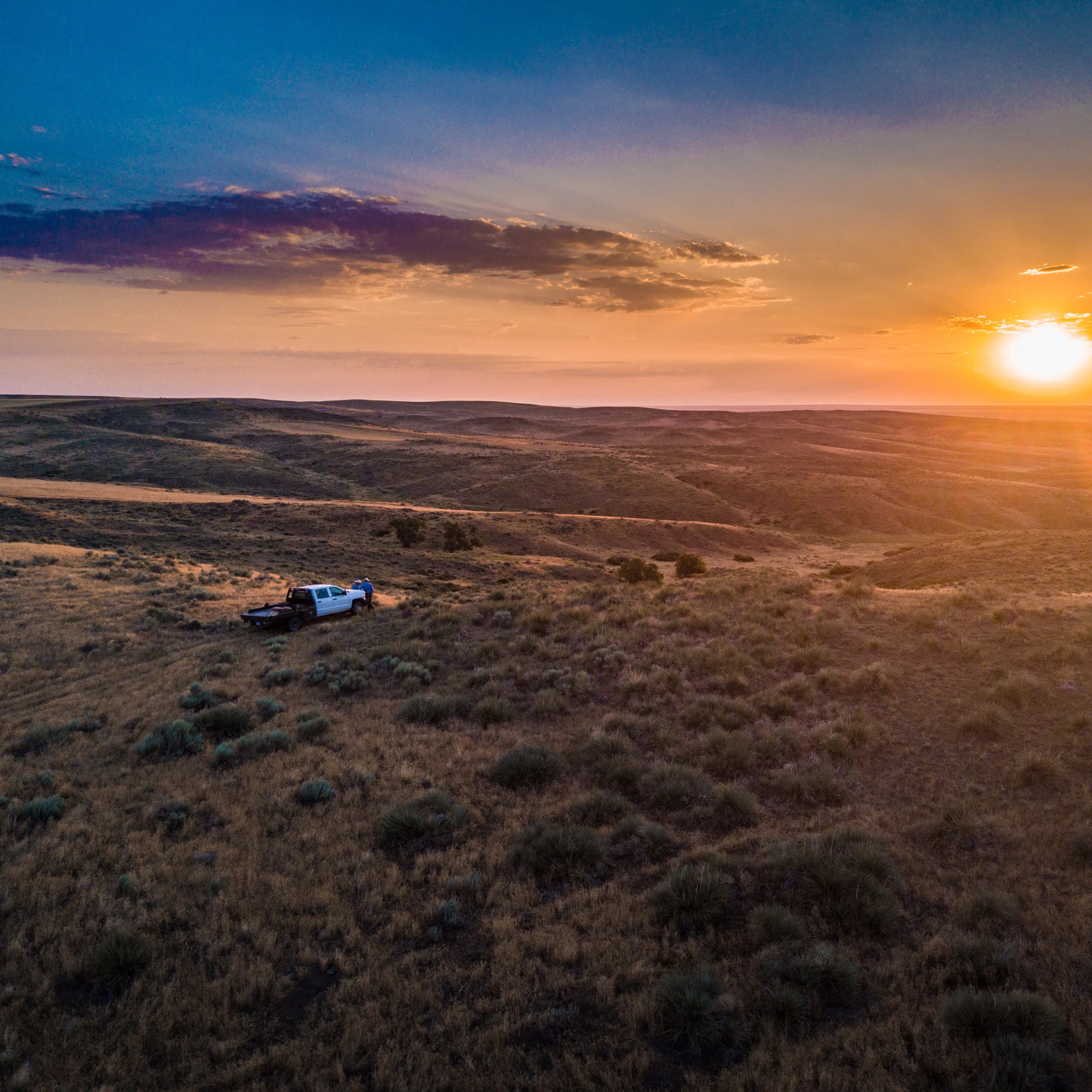A truck in a field overlooking hills with the sun setting