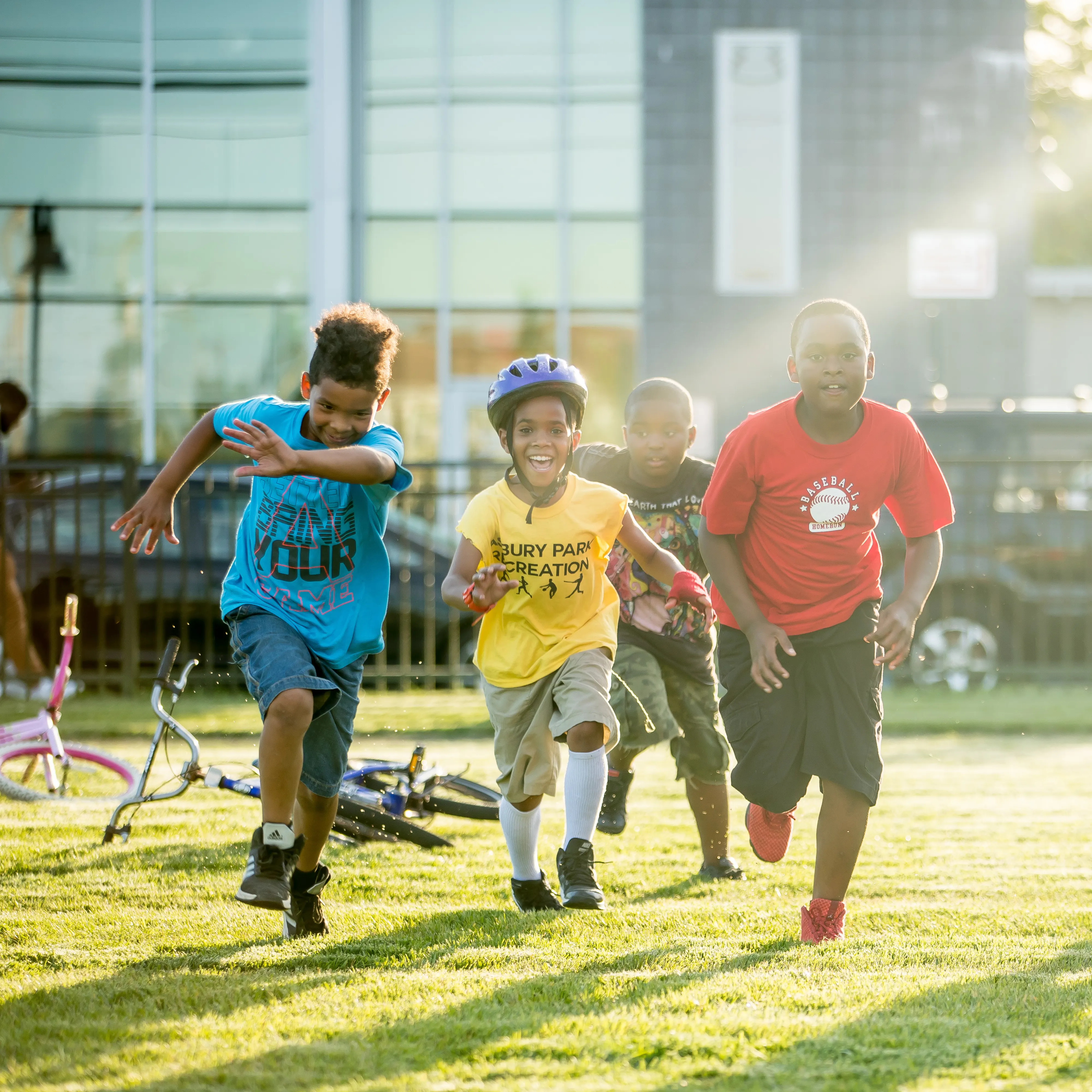 Children running and laughing, one with a bike helmet on.