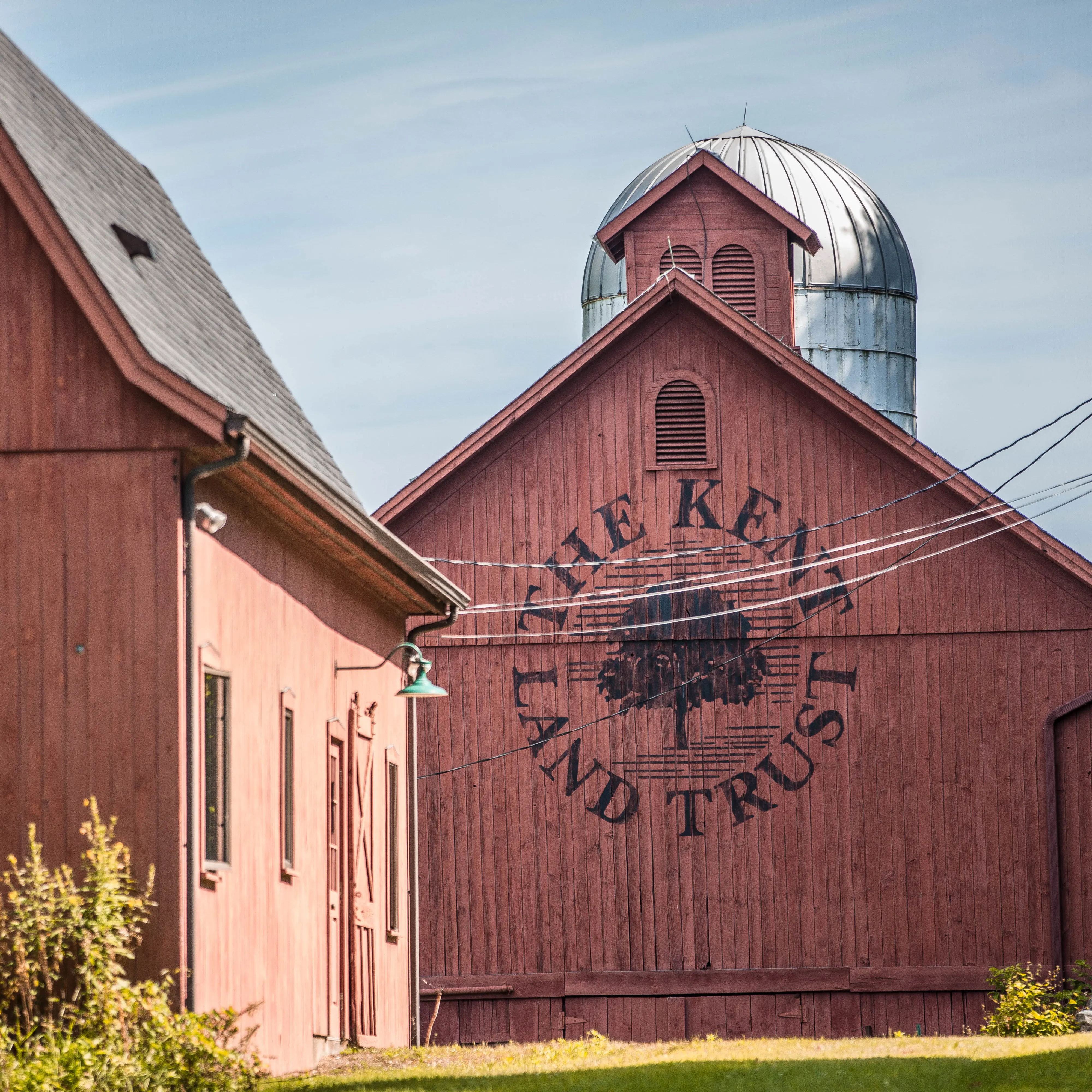 A red barn with the words "The Kent Land Trust" written on it surrounding a drawing of a tree.