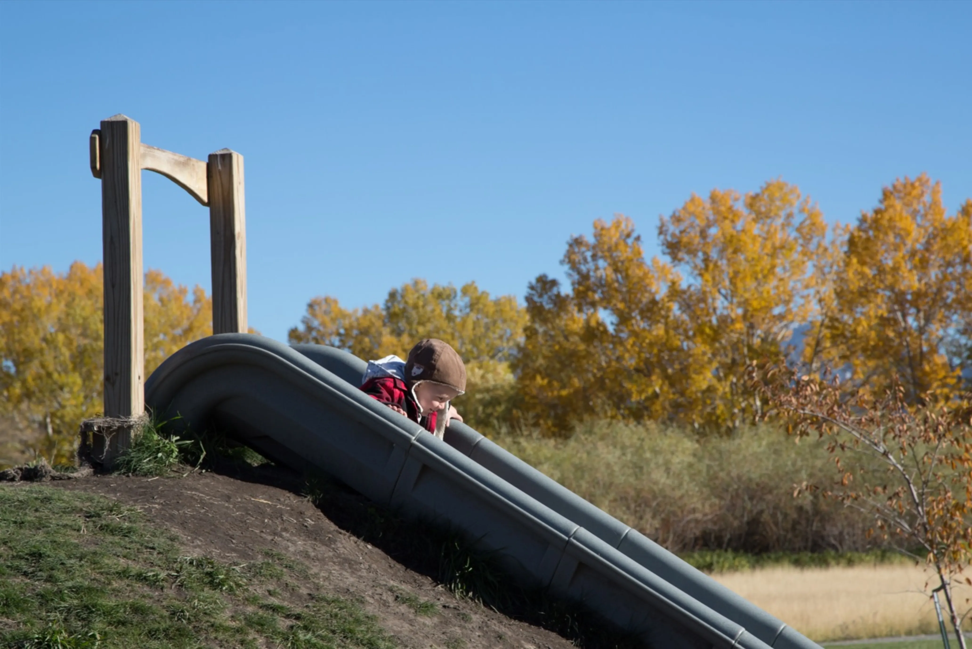 A young child slides down a slide on a land trust property in fall.