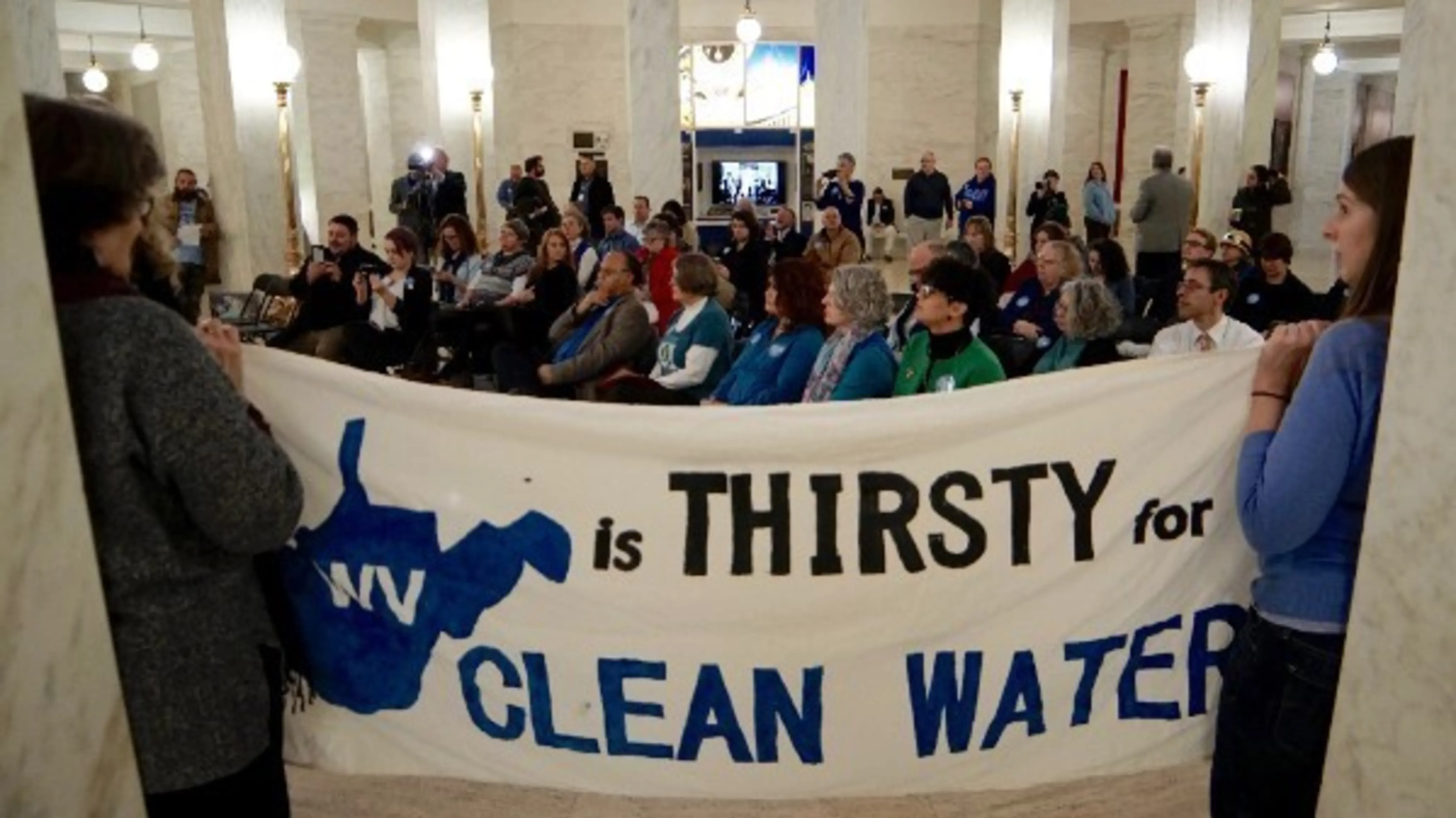 Advocates gather in the West Virginia capital building to rally for clean water. A sign says WV is thirsty for clean water.