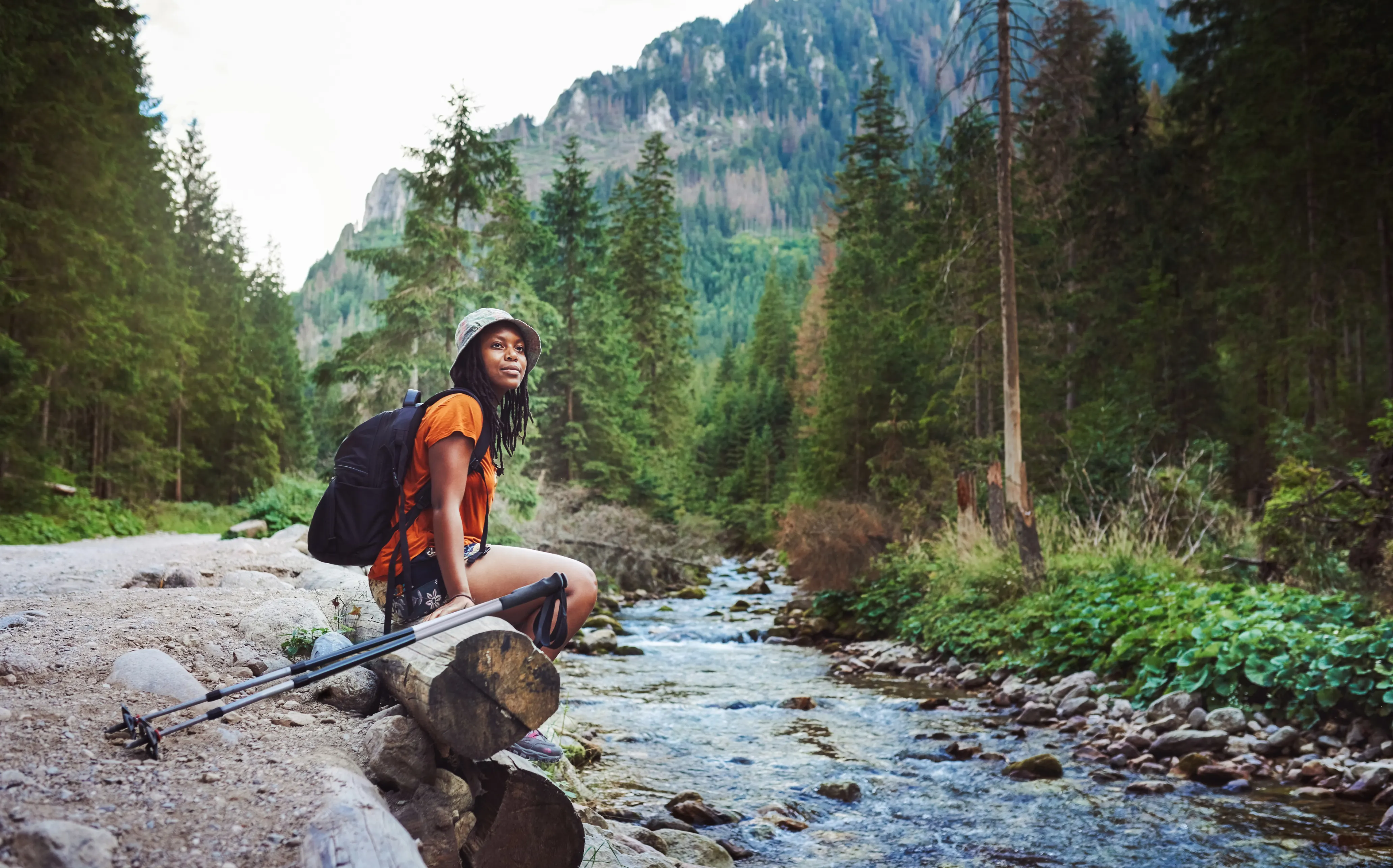 Black female presenting hiker sitting by stream