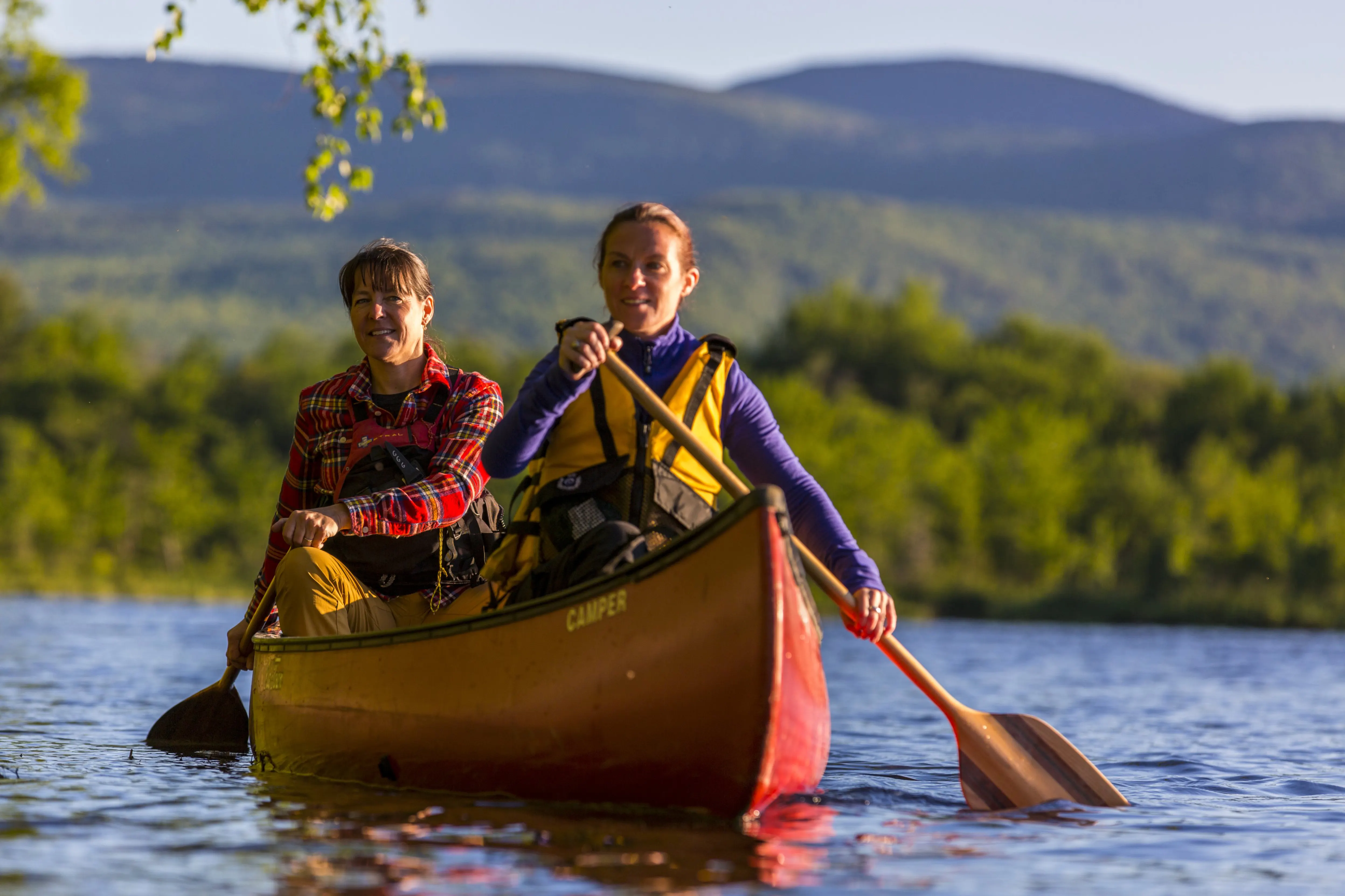 Two people in a canoe rowing on opposite sides, with mountains in the background.