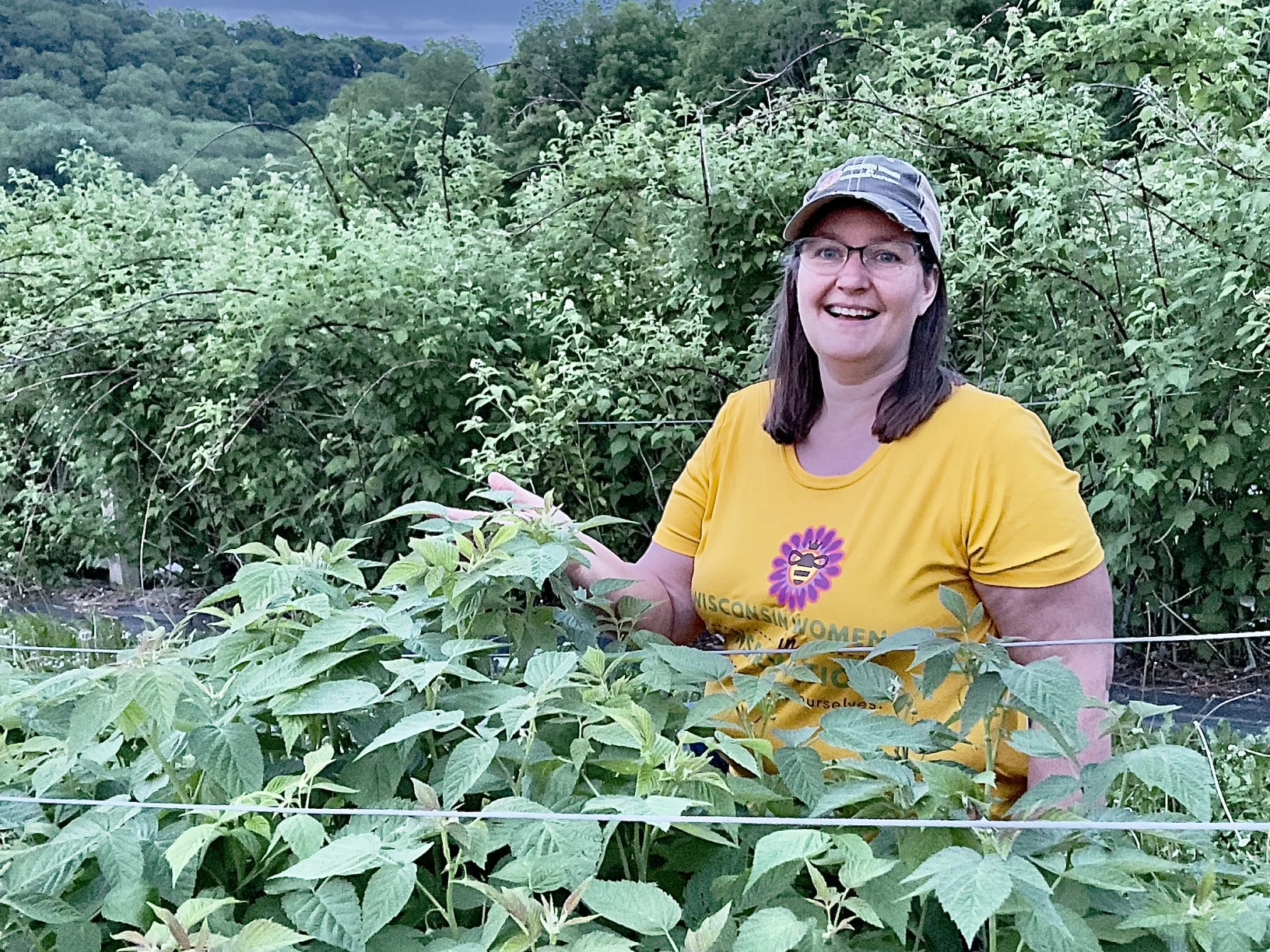 Woman wearing a shirt that says "Wisconsin Women in Conservation"  standing behind a large plant.