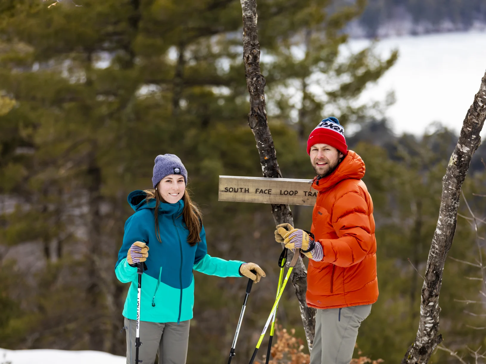 Two people skiing and smiling at the camera, in front of a sign that says South Face Loop Trail