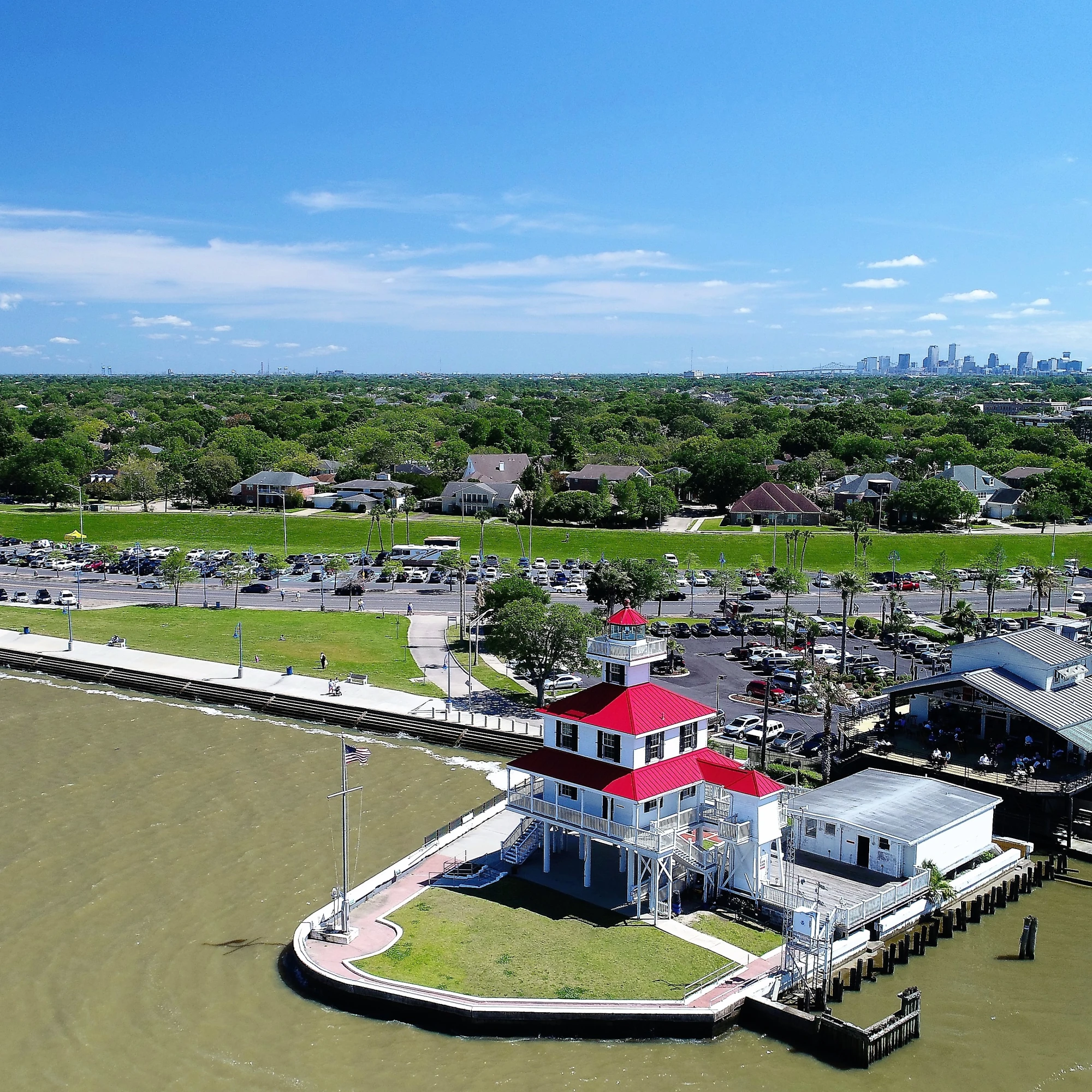 An above view of green water surrounded by a boardwalk with large buildings and boats in the water. In the distance there is a city skyscape