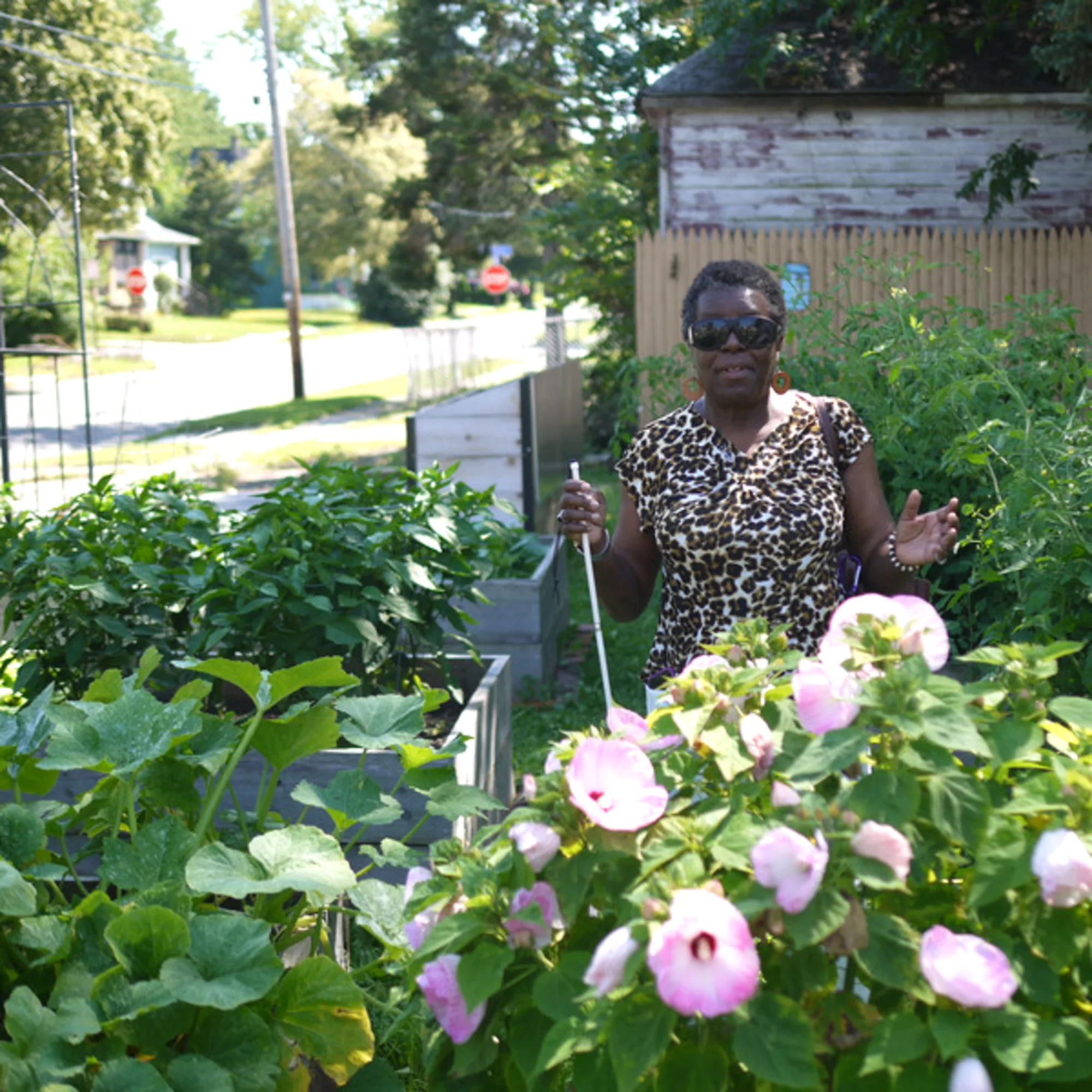 Woman standing in a garden wearing sunglasses and holding a probing cane.