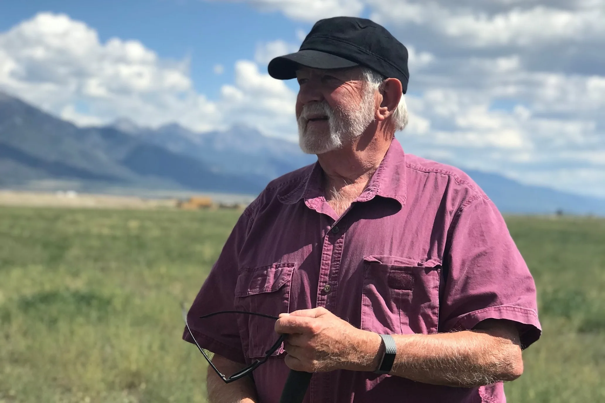 A farmer stands surveying a field as the sun shines onto him with mountains in the background.