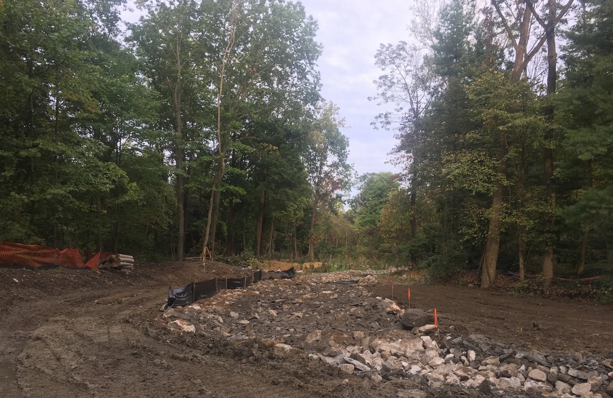 Preparation for development, flattened earth and broken rock surround by construction fencing and trees.