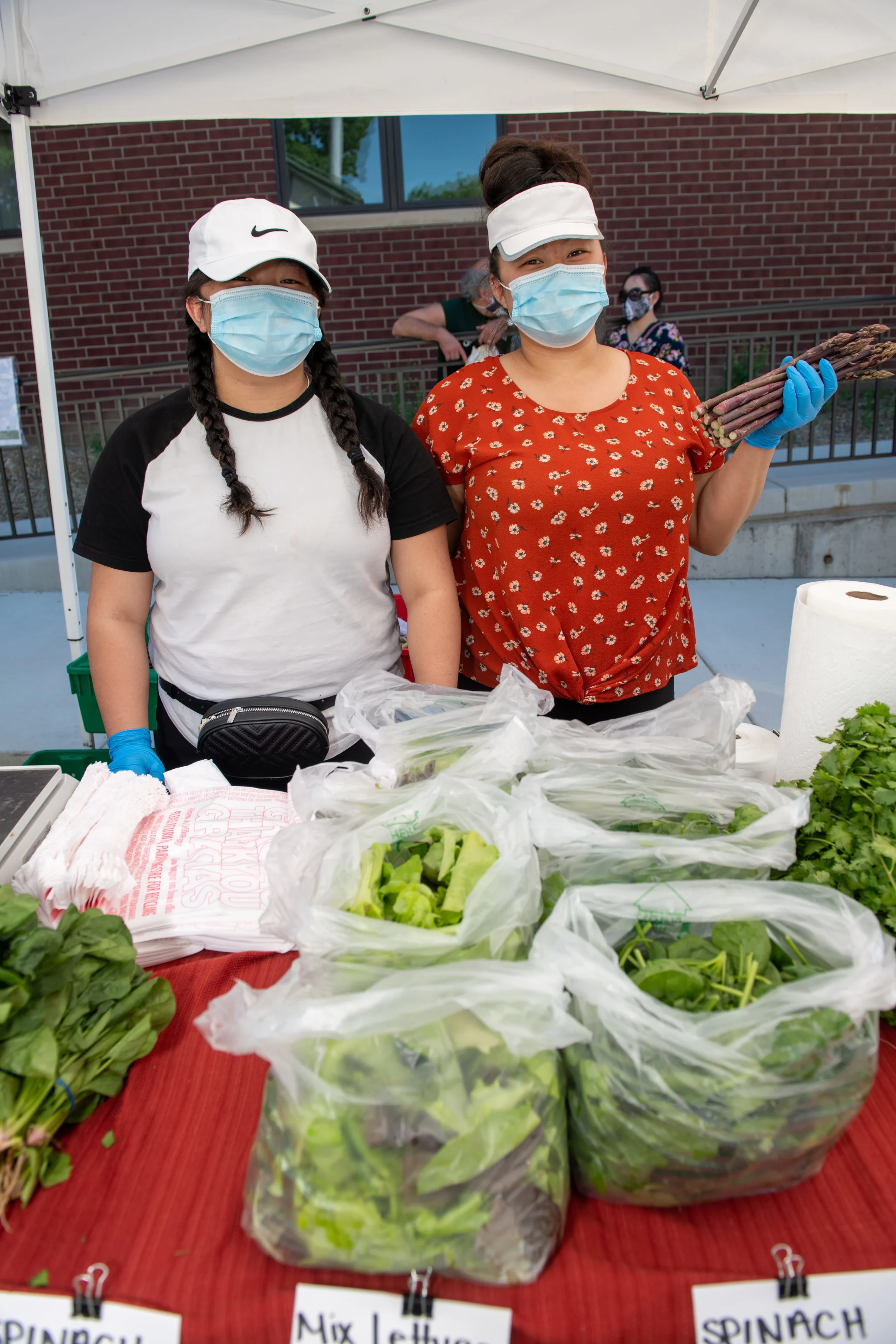 Two women Hmong farmers selling greens and vegetables at farmer's market.