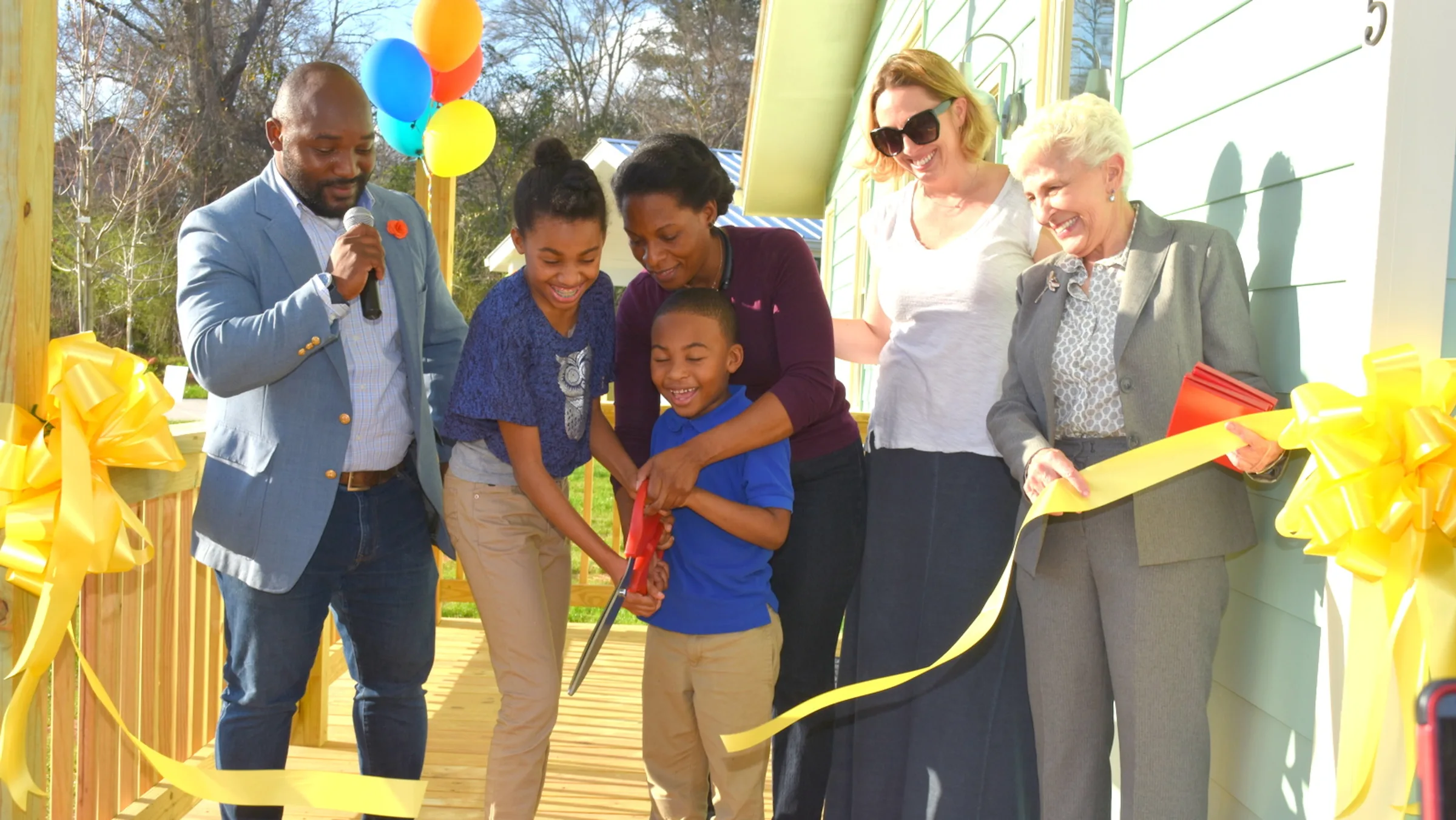 A young boy cuts a ribbon at a celebration for a new home. 