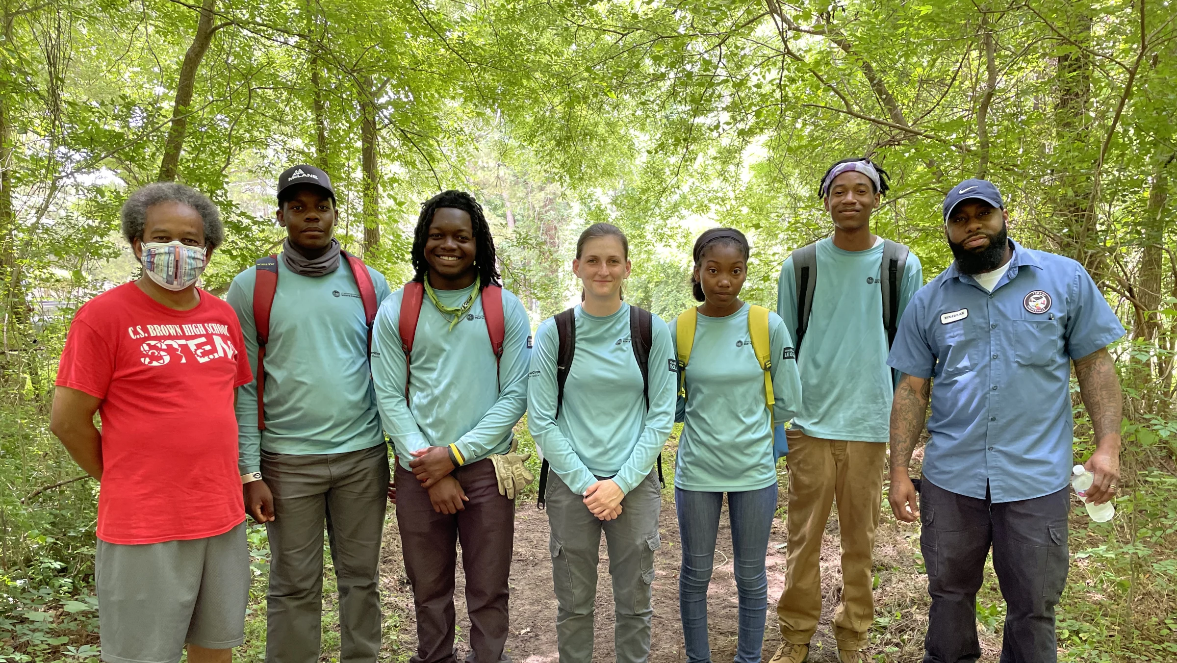 A youth trail crew stand in a group with their supervisors on a trail in the woods they helped build.