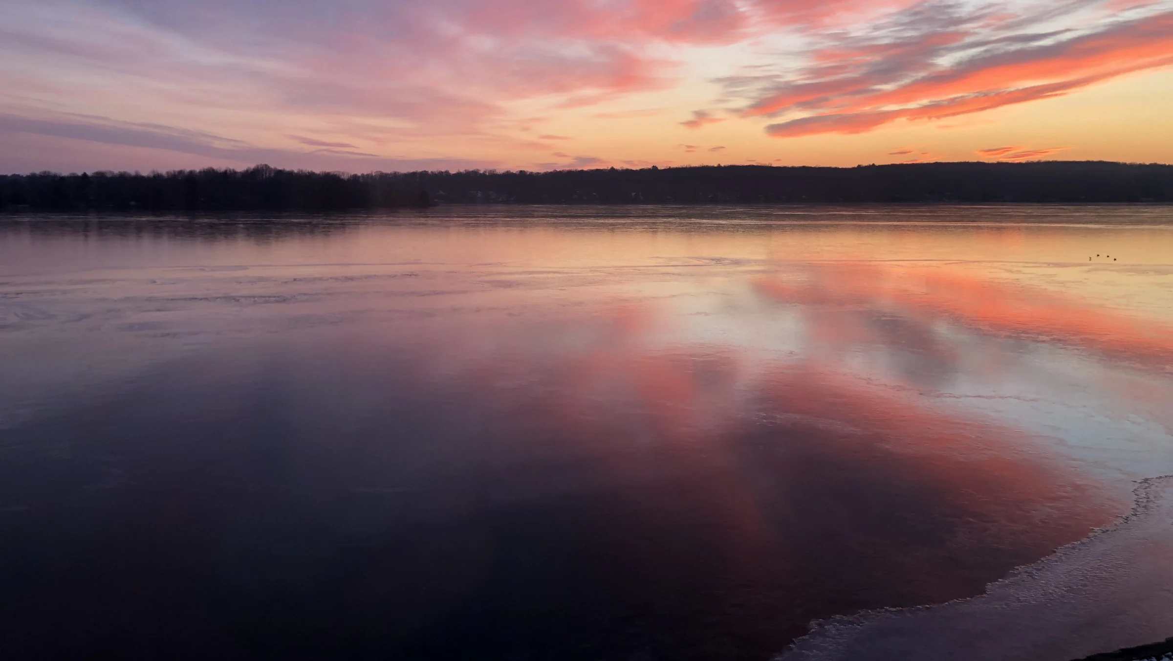Pink and orange clouds over a body of water surrounded by trees