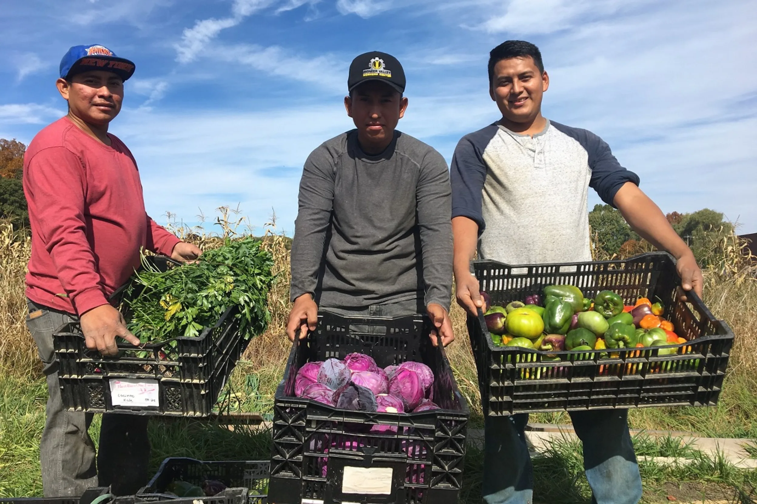 Family members stand side by side holding bins of different vegetables grown on their farm plots.