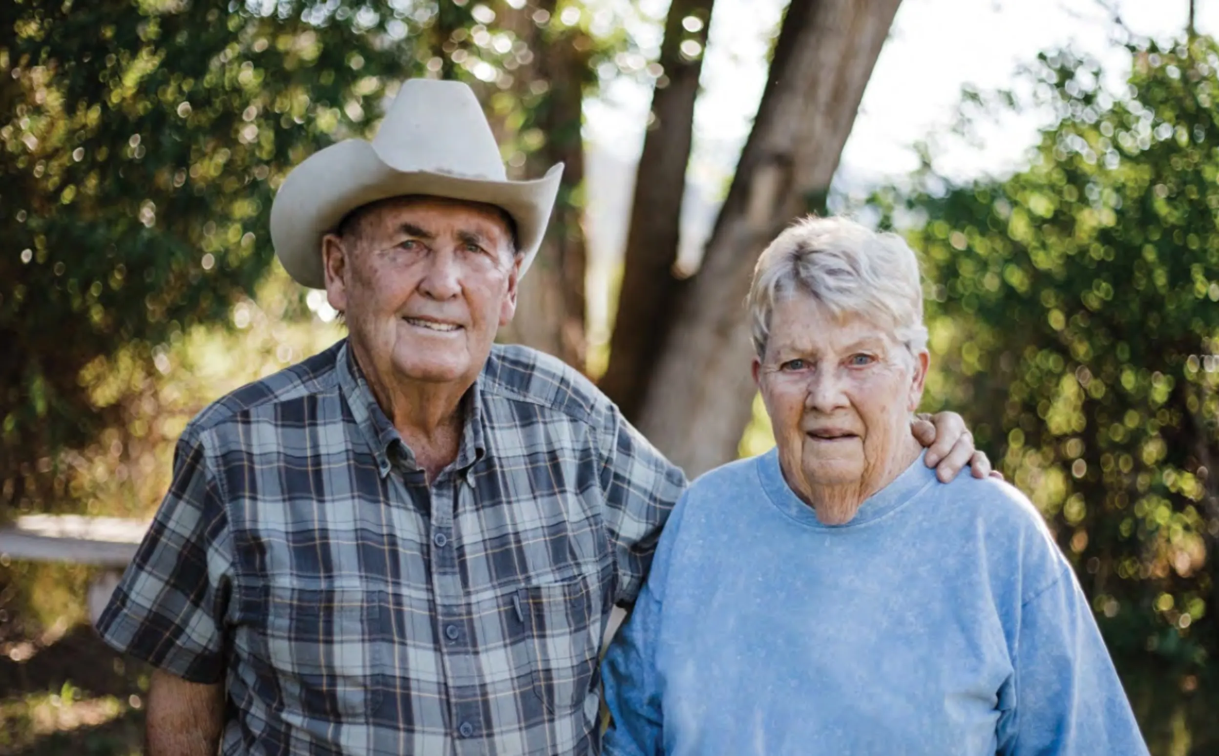 An older white man, a cowboy hat on his head, stands with his arm on his wife's shoulder.