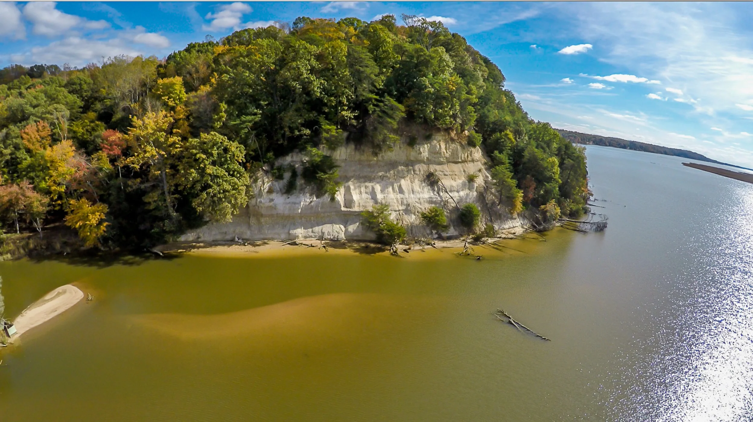 A sheer rockface topped by thick forest rises above a calm river, the Rappahannock River in Virginia.