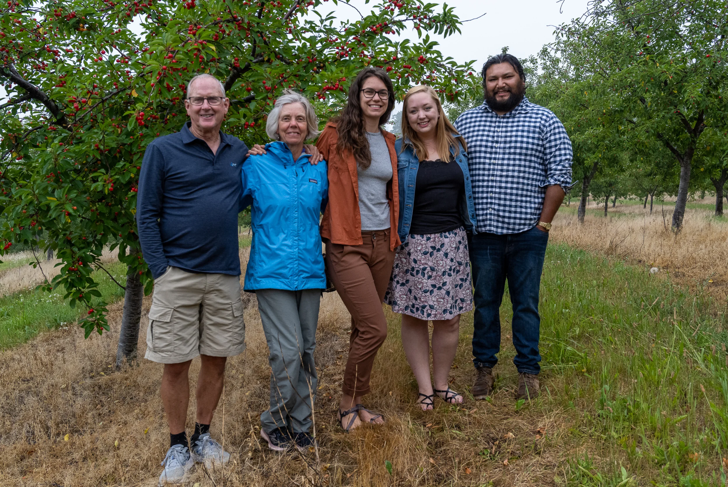 Five people standing with arms around each other in front of a tree with red berries on it.