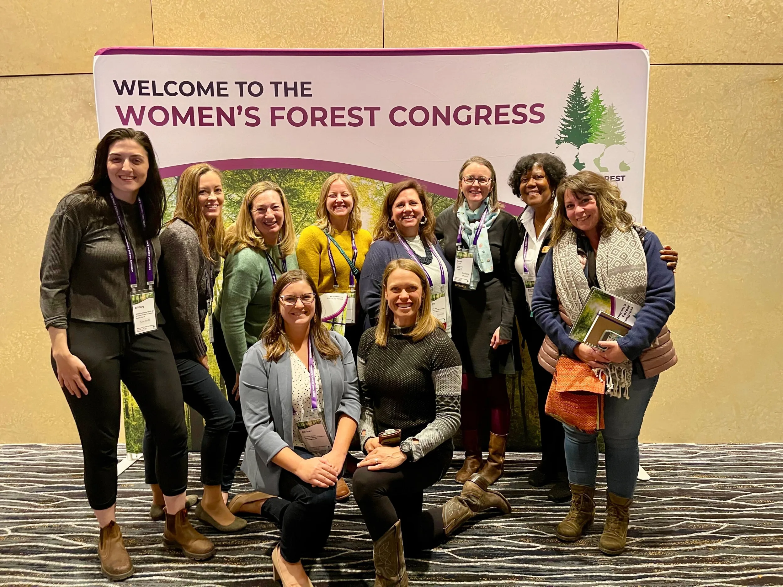 Ten women posing and smiling in front of a banner that says "Women's Forest Congress"