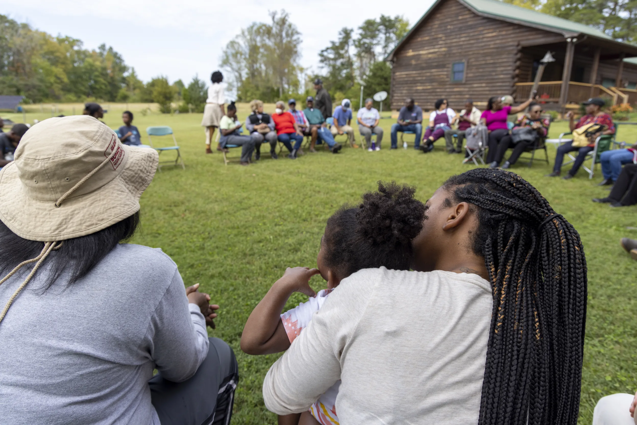 People sitting in a large circle in front of a cabin