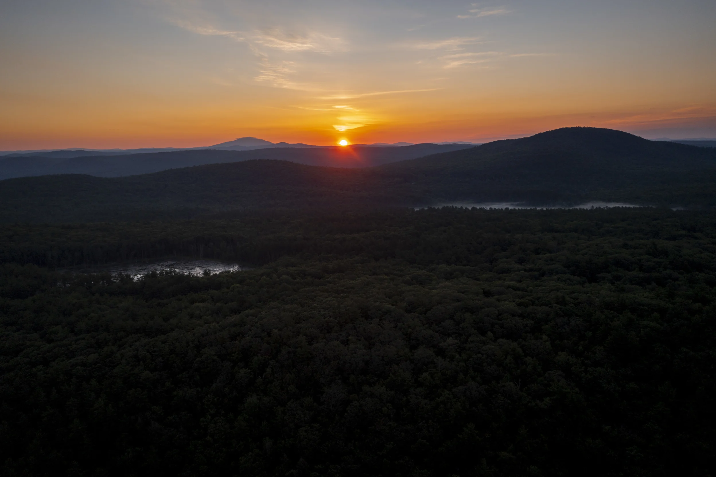 Sun rising over mountains with forest of trees in front.