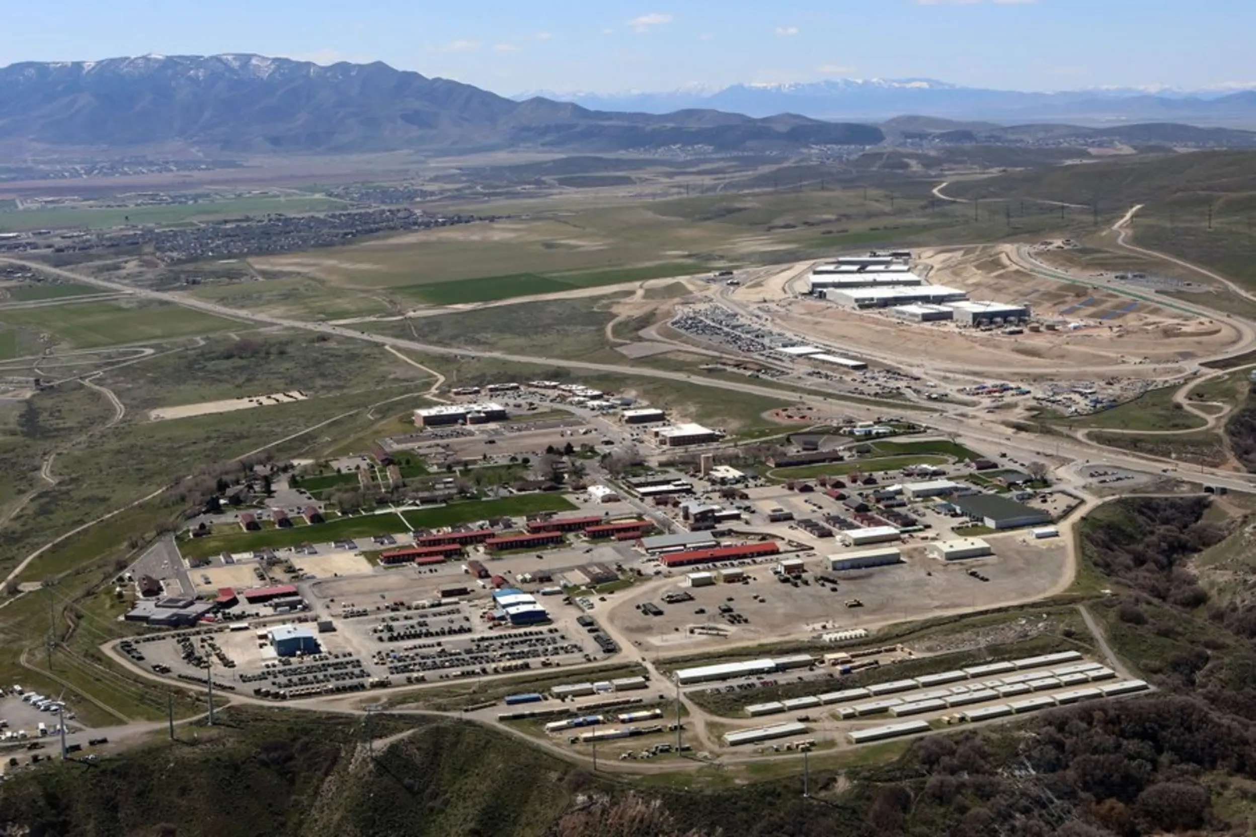 Photo taken from above of a military complex with many buildings and cars, surrounded by forest and mountains.