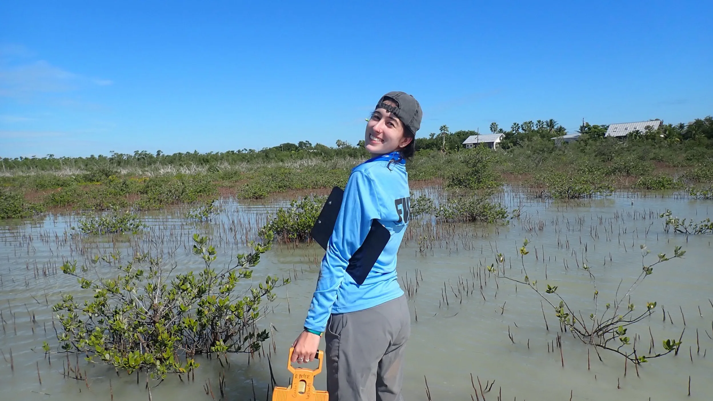 A young female marine biologist stands calf-deep in a coastal wetland.